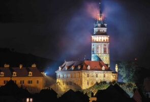 Illuminated Ceský Krumlov castle tower at night with a mist around it